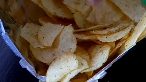 Kartoffel-Chips-im-Paket-auf-den-Tisch.-Weibliche-Hand-nimmt-chips