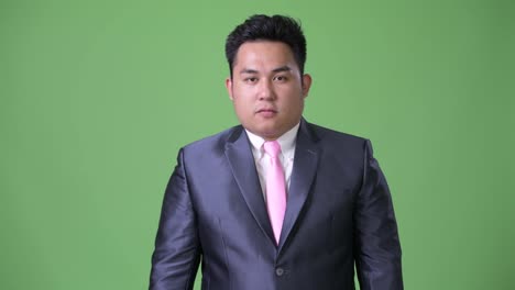 Young-handsome-overweight-Asian-businessman-against-green-background