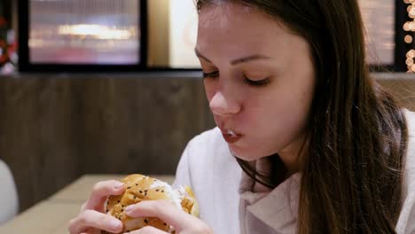 Woman-eating-a-hamburger-with-relish-and-delight-in-cafe.