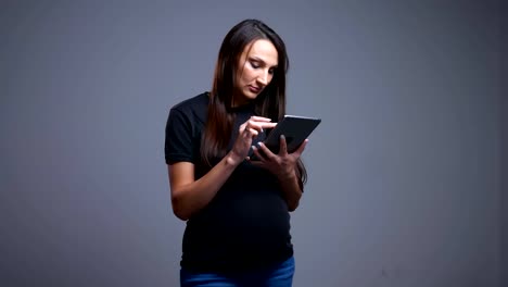 Nahaufnahme-von-schwangeren-jungen-kaukasischen-Frauen-tippt-auf-dem-Tablet-mit-Blick-auf-die-Kamera-und-lächelt