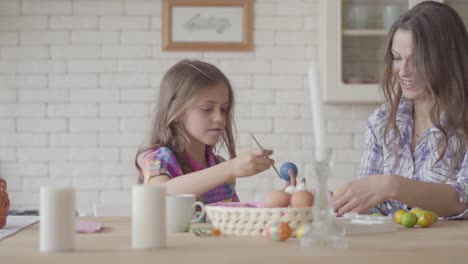 Cute-little-smiling-girl-painting-Eastern-eggs-with-a-small-brush-with-her-mom