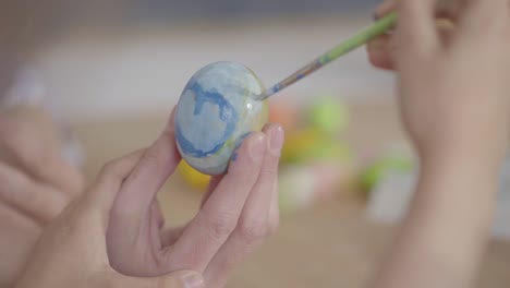 Unrecognized-little-girl-painting-a-heart-on-the-Easter-egg-using-a-small-brush-close-up.