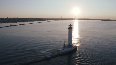 Toma-aérea-de-faro-blanco-cerca-del-puerto-marítimo-durante-el-atardecer,-silueta