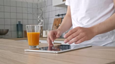 Attractive-man-at-home-using-tablet-in-kitchen-sending-message-on-social-media-smiling-enjoying-modern-lifestyle-wearing-white-shirt