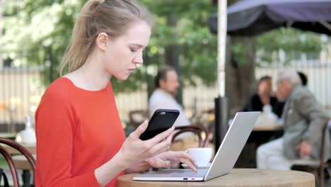 Young-Woman-Using-Smartphone-and-Laptop-Sitting-in-Cafe-Terrace