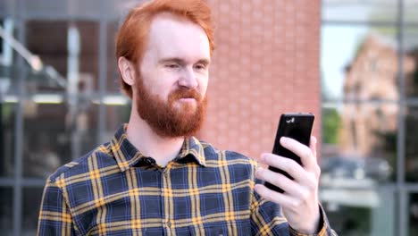 Outdoor-Redhead-Bart-junger-Mann-begeistert-für-Erfolg-auf-Smartphone