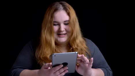 Closeup-shoot-of-young-overweight-caucasian-female-typing-on-the-tablet-and-reacting-to-social-media-posts-with-background-isolated-on-black