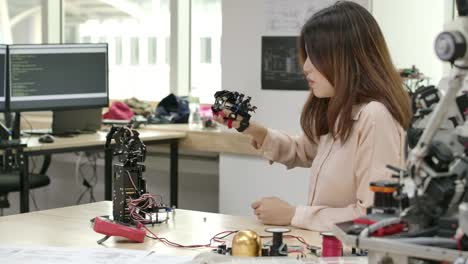 Young-creative-engineer-testing-innovative-robotic-technology-in-laboratory.-Young-asian-female-creates-movement-for-mechanical-robotic-hand.-People-with-technology-or-innovation-concept.