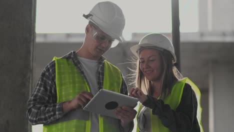 Bauarbeiter-Mann-und-Architekt-Frau-in-einem-Helm,-diskutieren-den-Plan-des-Baus-des-Hauses,-erzählen-einander-über-den-Entwurf,-halten-eine-Tablette,-Blick-auf-die-Zeichnungen,-Hintergrund-der-Sonnenstrahlen