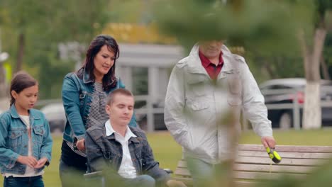 Parents-go-with-children-in-the-city.-Guy-in-a-wheelchair-goes-with-his-parents-and-sister-along-the-avenue,-a-dog-runs-alongside.