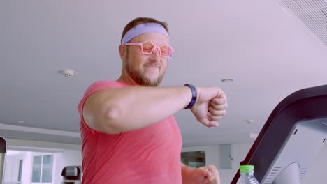 Funny-fat-male-in-pink-glasses-and-in-a-pink-t-shirt-is-engaged-on-a-treadmill-in-the-gym-depicting-a-girl.-4k