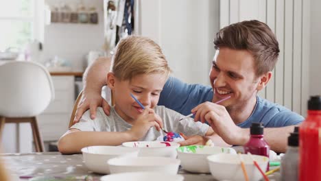 Father-sitting-at-kitchen-table-helping-son-to-paint-eggs-for-Easter---shot-in-slow-motion