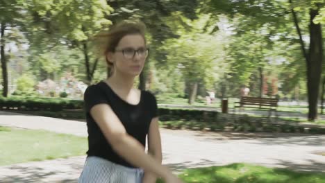 Mujer-caucásica-bastante-joven-en-anteojos-caminando-hacia-la-cámara,-revisando-el-teléfono-y-celebrando-buenas-noticias-en-un-parque