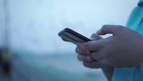 Mujer-asiática-jugando-teléfono-inteligente-en-el-puerto-con-un-poco-de-puesta-de-sol-fría-de-fondo.-A-cámara-lenta.