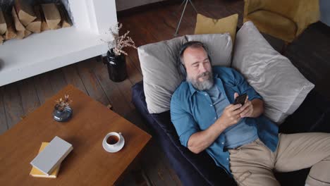 Aged-Man-Listening-to-Podcast-Lying-on-Sofa