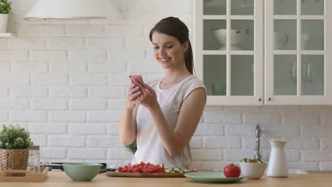 Lächelnde-junge-Frau-bereitet-gesunden-Gemüsesalat-mit-mobilen-Apps-zu