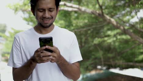 Joven-asiático-caminando-y-disfrutando-de-smartphone-al-aire-libre