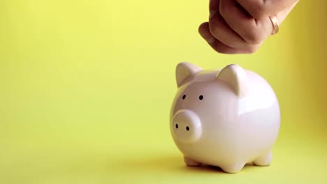 Man's-hand-putting-coins-in-piggy-bank-of-pig-shape-on-yellow-background