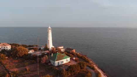 Lighthouse-on-the-cape.-beautiful-shot-from-the-air,-flying-over-the-lighthouse-during-sunset,-beautiful-light,-scenic-landscape-sky-and-sea,-Suristic-colors.-Flying-around-the-lighthouse