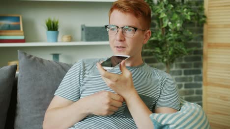 Joven-feliz-grabando-mensaje-de-voz-sonriendo-usando-el-teléfono-inteligente-en-casa