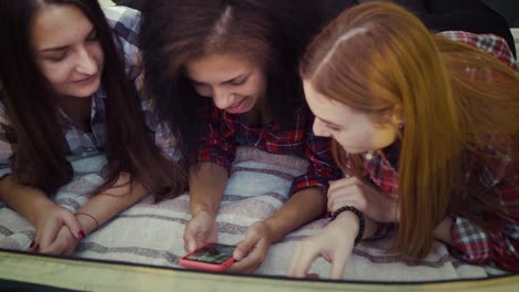 Chicas-alegres-relajándose-en-la-manta-y-el-uso-de-teléfono-inteligente-para-la-diversión