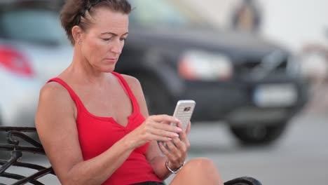 Madura-mujer-turista-feliz-usando-el-teléfono-mientras-está-sentada-en-el-banco