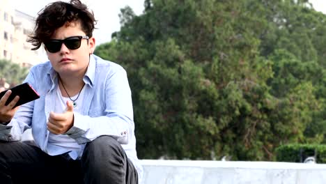 Teenage-boy-sitting-at-the-outdoor-with-smartphone