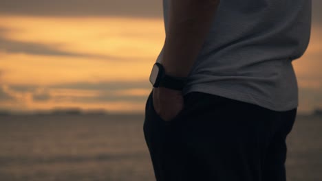 Nah-aufnahme-stattlich-Mann-Läufer-trägt-eine-Smartwatch,-während-stehen,-um-Blick-auf-den-Strand-während-eines-schönen-Sonnenuntergangs-im-Sommer-zu-sehen.