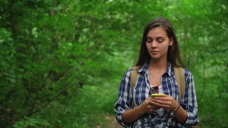 Young-female-is-walking-in-wood,-holding-cellphone