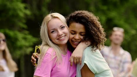 Positive-female-couple-in-love-hugging-cheek-to-cheek,-looking-into-cam-at-party