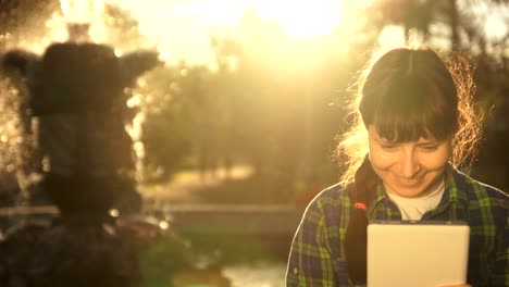 Eine-Frau-benutzt-eine-weiße-Tablette-am-Brunnen-im-Sommer-bei-Sonnenuntergang.