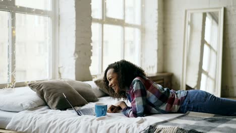 Attractive-mixed-race-teenage-girl-lauging-using-laptop-for-sharing-social-media-lying-in-bed-at-home