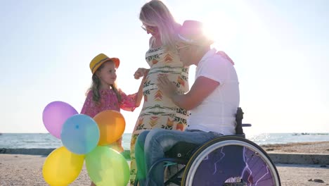 happy-mother-with-big-belly-communicates-with-daughter-and-husband-on-wheelchair,-pregnancy,-disabled-man