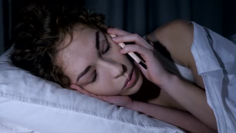 Close-Up-de-rostro-femenino,-hablando-por-teléfono-móvil-en-la-cama-por-la-noche