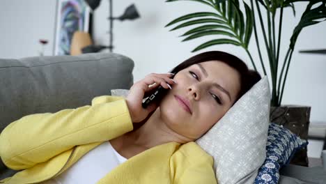 Joven-mujer-hablando-por-teléfono-mientras-tendido-en-el-sofá-en-casa