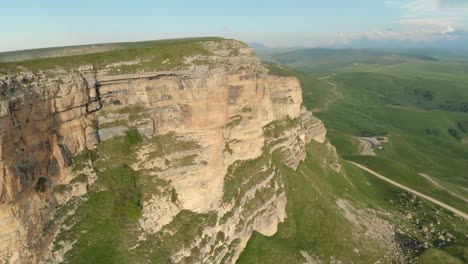 Antenne:-Flug-über-eine-hohe-Felswand,-offenbart-einen-Blick-des-Passes-in-Russland-im-Nordkaukasus.-Luftaufnahmen-von-der-Straße-in-der-untergehenden-Sonne.-Flug-neben-dem-Felsen