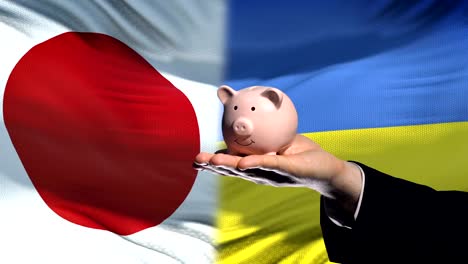 Japan-Investitionen-in-der-Ukraine,-Hand,-Geld-im-Sparschwein-auf-Flagge-Hintergrund