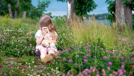 Una-niña-jugando-con-un-conejo-de-juguete-en-el-Prado-entre-el-trébol-de-flores