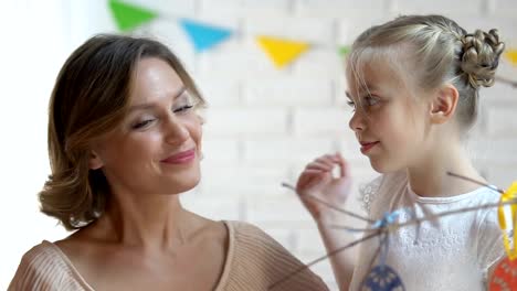 Mother-and-daughter-decorating-branches-with-hand-made-toy-eggs-on-Easter-eve