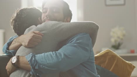 Cute-Attractive-Male-Gay-Couple-Sit-Together-on-a-Sofa-at-Home.-Boyfriends-are-Hugging-and-Embracing-Each-Other.-They-are-Joyful-and-Laughing.-They-are-Casually-Dressed-and-Room-Has-Modern-Interior.