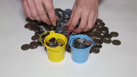 Girl's-hands-putting-coins-in-small-colorful-buckets