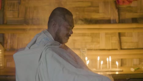 Asian-man-in-authentic-temple-while-religion-ritual-on-burning-candle-background.-Happy-man-hope-on-healing-while-magic-ceremony-in-magic-house.-Esoteric-tradition-and-healing.