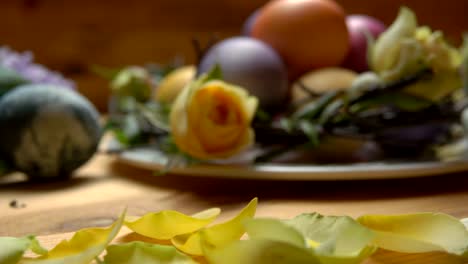 Petals-of-a-yellow-rose-fall-on-a-table-with-Easter-eggs