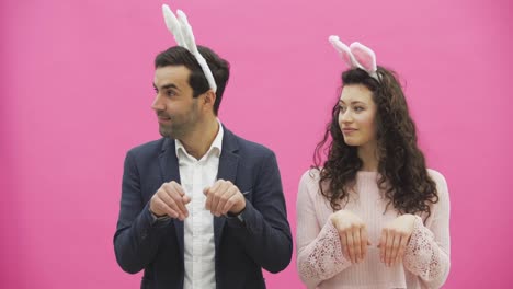 Young-couple-standing-standing-on-pink-background.-During-this-time,-they-are-dressed-in-rabble-ears.-Looking-gently-at-each-other,-rhythmically-simultaneously-turning-his-head-to-the-side.-Easter.