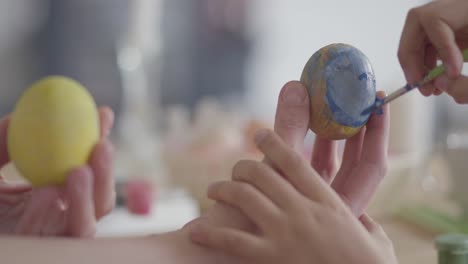 Close-up-of-mother-and-daughter-hands-coloring-easter-eggs-with-colors-and-brush.