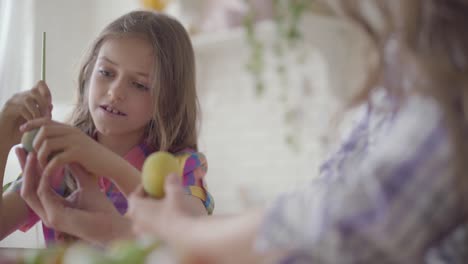 Female-hand-holding-Easter-egg-while-girl-painting-on-it-a-heart-with-a-brush-close-up.