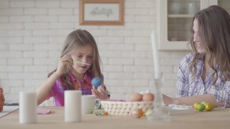 Cute-little-smiling-girl-painting-Eastern-eggs-with-a-small-brush-with-her-mom