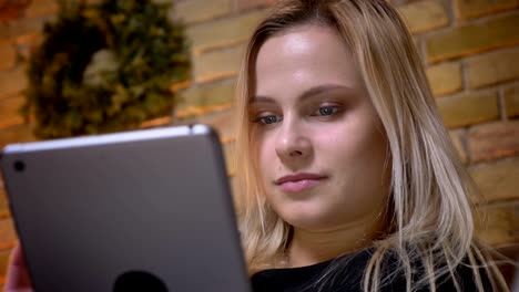 Retrato-en-primer-plano-de-mujer-joven-con-cabello-rubio-usando-la-tableta-en-el-interior-de-la-acogedora-casa