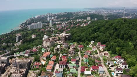 Luftvideos.-Panoramablick-aus-der-Höhe-der-Stadt-Sotschi.-Grüne-Bäume-und-Berge-am-Meer.-wohngebiet.-Hohe-Häuser-am-Strand.-Blauer-und-klarer-Himmel.