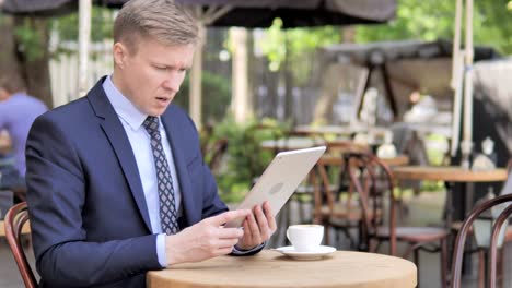 Businessman-Upset-by-Loss-on-Tablet,-Sitting-in-Outdoor-Cafe